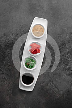 Set of sauces for sushi on a white plate, ginger, soy, sesame, seaweed. dark gray textured background, top view