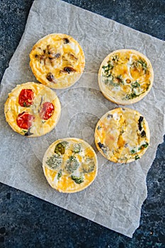 Set of savory mini tarts on a baking paper. Vegetable quiches wi