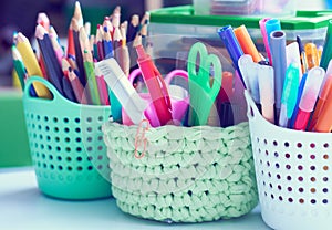 Colored pencils, pens, basket with flowers, watercolor paints and other items on wooden desk. Back to school concept.