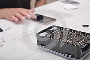 set of screwdriver bits in a black box close-up, a man checks a phone he has repaired, smartphone repair concept