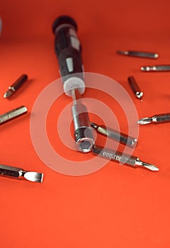 A set of a screwdriver with replaceable bits and bits for her for working with small parts on a red background