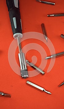 A set of a screwdriver with replaceable bits and bits for her for working with small parts on a red background