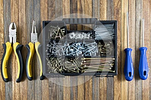 set screws in plastic case, screwdriver and pliers on wooden background