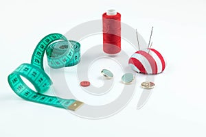 Set of sewing accessories: A green measuring centimetric tape l , the scattered buttons, the coil of red threads on a white photo