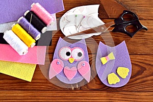 Set for sewing a felt owl, paper templates, felt sheets, scissors, thread, needle, pins on a brown wooden background