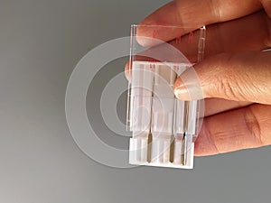 A set of sewing machine needles in a white plastic case. A woman`s hand holds the needles for an electric sewing machine