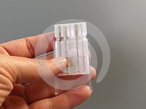 A set of sewing machine needles in a white plastic case. A woman`s hand holds the needles for an electric sewing machine. Gray