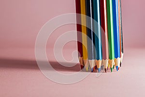 A set of sharpened multi-colored pencils, standing on a light pink background on the right side, with a clear shadow from the