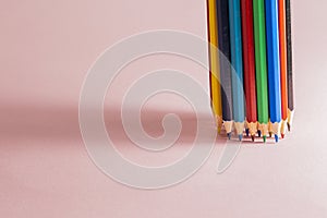 A set of sharpened multi-colored pencils standing on a light pink background on the right side, with a slight shadow. Horizontal