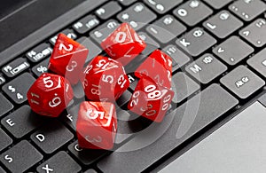 Set of simple red RPG role playing fantasy board game dice laying on a modern laptop computer keyboard, closeup, from above