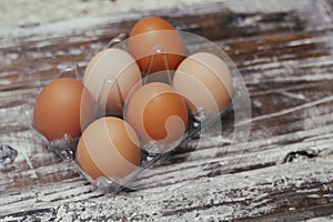 Set of six fresh brown eggs on clear plastic box. Wooden table background.