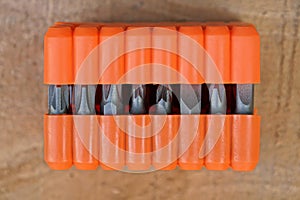 Set of metal bits for a screwdriver in an orange plastic box on the table
