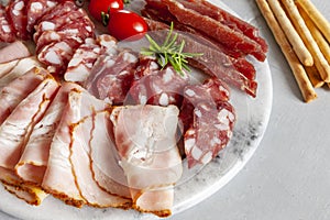 Set of smoked bacon, salami and basturma served with omatoes and grissini bread. Close up, top view on white background