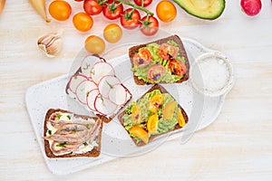 Set of smorrebrods with fish, anchovies, avocado, tomatoes, radish. Top view, white board, white background