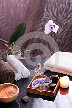 Set for spa procedures on the table, terry towels, bath salts, massage stones and bio-oil. Flowering orchid in the