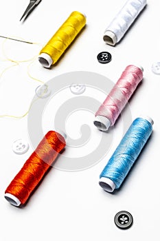 Set of spools of colored thread with a threaded needle, black and white buttons on a white background