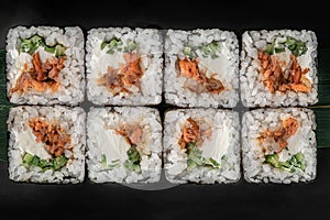 Set of square maki rolls with fried salmon, curd cheese and green bamboo leaf in a black ceramic plate with chopstick on a dark