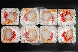 Set of square maki rolls with tiger shrim, caviar and green bamboo leaf in a black ceramic plate with chopstick on a dark gray