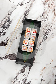 Set of square maki rolls with tiger shrimp, caviar and green bamboo leaf in a black ceramic plate with chopstick on a bright