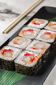 Set of square maki rolls with tiger shrimp, caviar and green bamboo leaf in a black ceramic plate with chopstick on a bright