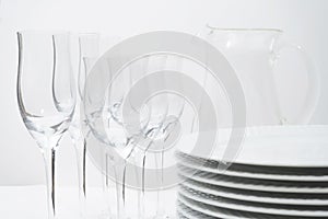 Set of stacked white plates, crystal stemware and a glass jug on a white table