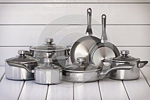 Set of stainless pots and pan with glass lids on the white wooden background