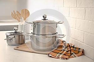 Set of stainless steel cookware and kitchen utensils on table near white brick wall