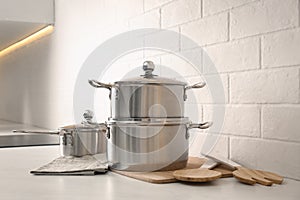 Set of stainless steel cookware and kitchen utensils on table near white brick wall