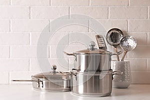 Set of stainless steel cookware and kitchen utensils on table near white brick wall, space for text