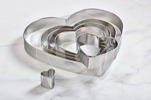 Set of stainless steel heart-shaped cookie cutters on a white marble surface