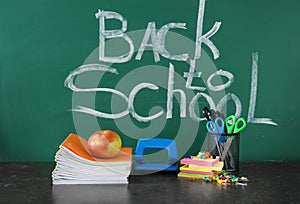 Set of stationery on table and words BACK TO SCHOOL written on chalkboard