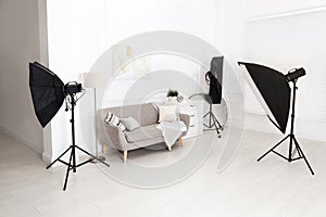 Set of stylish furniture surrounded by professional lighting equipment in photo studio. Cozy living room interior imitation