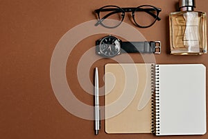 Set of stylish male accessories with a pen, perfume, clock, notepad and glasses on brown background. Minimal concept Fathers Day