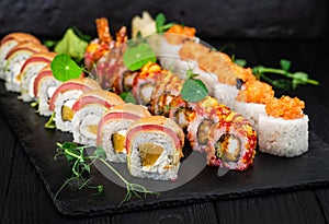 Set of sushi roll pieces on black slate stone plate with sprouts of fresh herbs