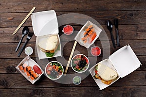 Set of sushi rolls  bao buns and poke in a plastic box on a wooden table. Pan-Asian cuisine to go or delivery in a plastic