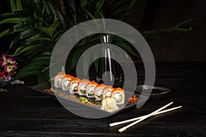 Set of sushi rolls on a black plate on a black wooden background with green leaves of a houseplant