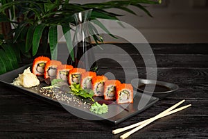 set of sushi rolls on a black plate on a black wooden background with green leaves of a houseplant