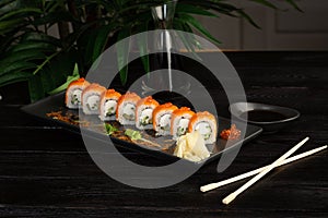 Set of sushi rolls on a black plate on a black wooden background with green leaves of a houseplant
