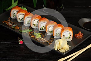 Set of sushi rolls on a black plate on a black wooden background with green leaves of a houseplant