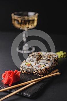 Set of sushi rolls on a black textured background served with wasabi and ginger