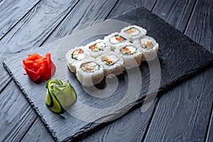 Set of sushi rolls with cream cheese, rice and salmon on a black board decorated with ginger and wassabi on a dark wooden