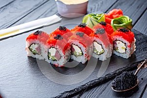 Set of sushi rolls with cream cheese, rice and salmon on a black board decorated with ginger and wassabi on a dark wooden