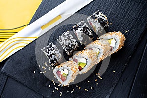 Set of sushi rolls with cream cheese, rice and salmon on a black board decorated with ginger and wassabi on a dark wooden