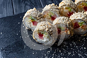 Set of sushi rolls with cream cheese, rice and tuna on a black board decorated with ginger and wassabi on a dark wooden background