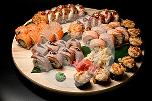 Set of sushi rolls on a round wooden board: tuna, trout and salmon rolls, fried tempura rolls