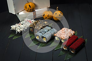 Set of Sushi rolls served in Halloween party style. Funny painted pumpkins near delivery boxes.