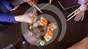 A set of sushi rolls on a table in a restaurant. A party of friends eating sushi rolls using bamboo sticks.