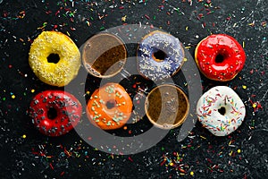 Set of sweet colored donuts with a cup of coffee on a black stone table.