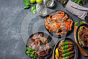 Set table with seafood dishes - cooked crabs, tiger shrimps, grilled octopus and squids on cast iron pan.