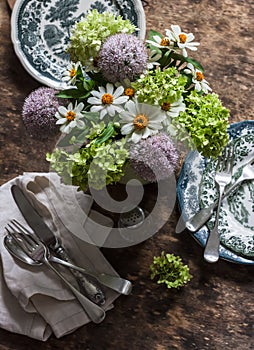 Set table with vintage dishes, silver cutlery, summer flowers, napkins on a wooden background, top view